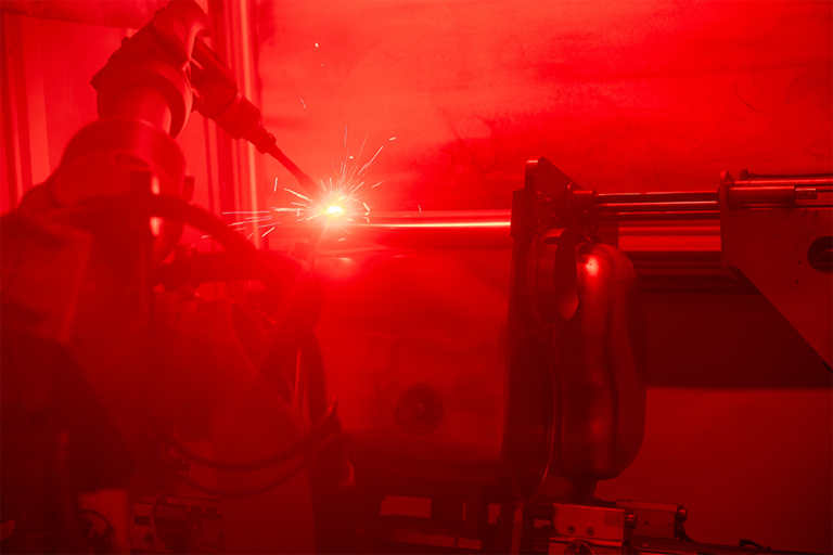 Ein Schweißroboter bei der vollautomatischen Arbeit hinter einem roten Schutzglas